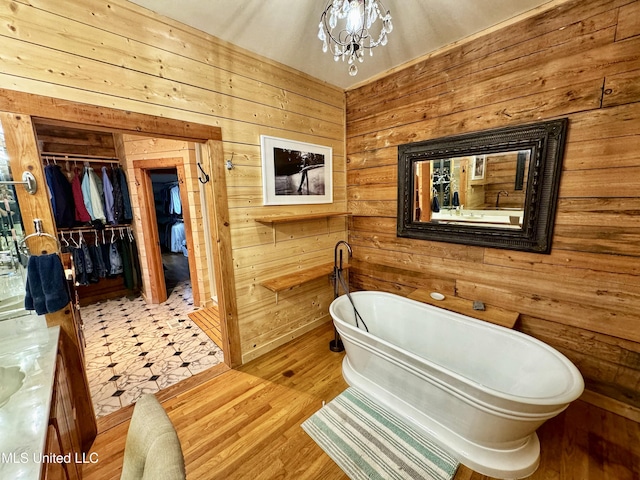 bathroom featuring a notable chandelier, wood walls, hardwood / wood-style floors, and a tub