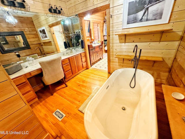 bathroom with hardwood / wood-style flooring, vanity, wooden walls, and a bathing tub