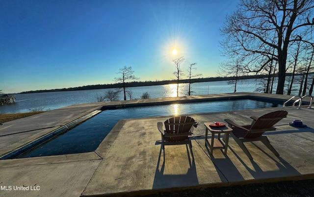 pool at dusk with a patio and a water view