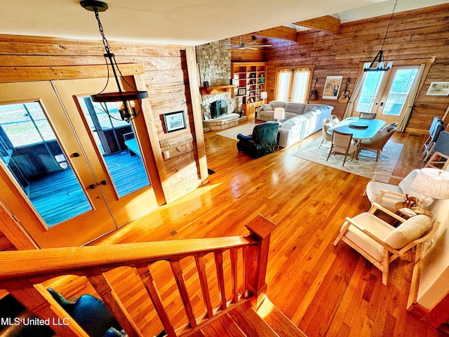 living room featuring french doors, wooden walls, hardwood / wood-style flooring, ceiling fan, and a fireplace