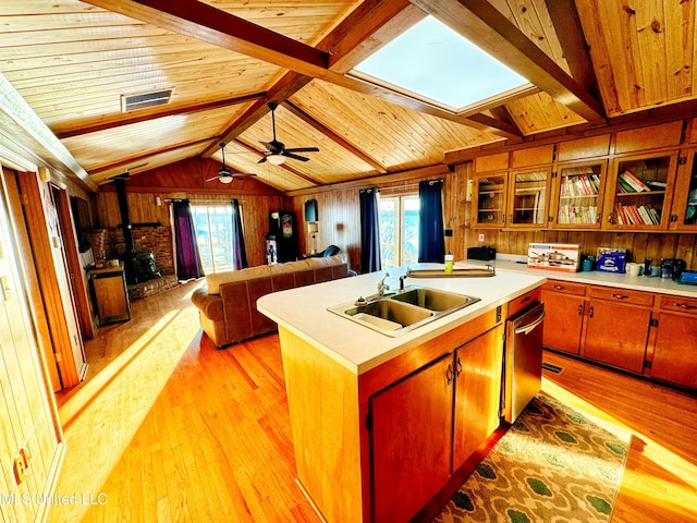 kitchen featuring wood walls, wood ceiling, light hardwood / wood-style flooring, a wood stove, and a kitchen island with sink