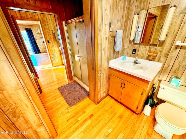 bathroom with wood walls, hardwood / wood-style flooring, vanity, an enclosed shower, and toilet