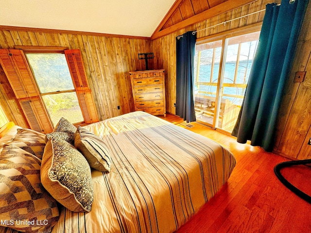 bedroom featuring vaulted ceiling, wooden walls, a water view, wood-type flooring, and access to outside