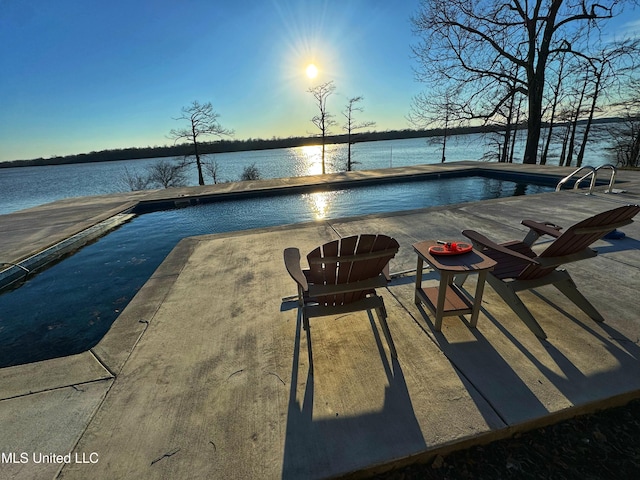 pool at dusk featuring a water view and a patio