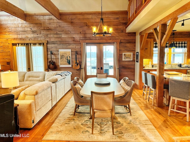 dining room with wooden walls, a notable chandelier, french doors, beamed ceiling, and light wood-type flooring