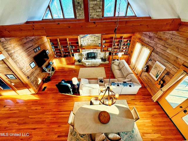 living room with a stone fireplace, high vaulted ceiling, hardwood / wood-style floors, and wood walls