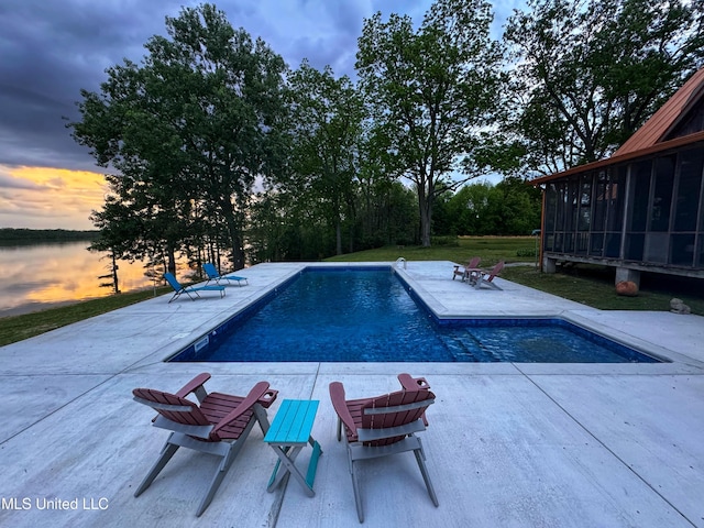 pool at dusk with a sunroom, a patio, and an outdoor pool