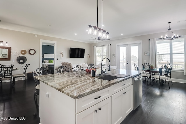 kitchen featuring sink, white cabinetry, hanging light fixtures, light stone counters, and an island with sink