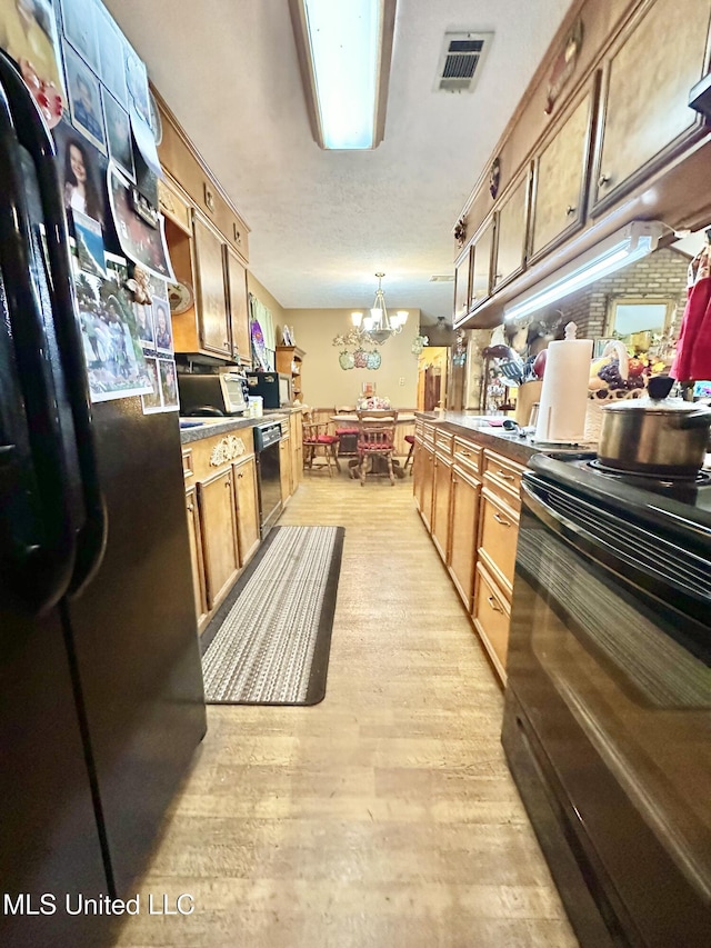 kitchen featuring light wood-type flooring, a textured ceiling, black appliances, pendant lighting, and an inviting chandelier