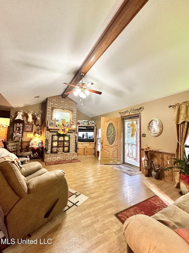 living room with a brick fireplace, a textured ceiling, ceiling fan, lofted ceiling with beams, and hardwood / wood-style floors