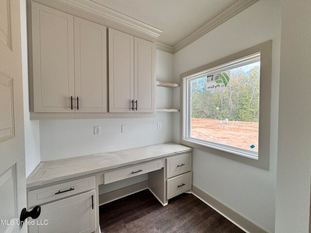 unfurnished office featuring dark wood-type flooring, built in desk, and ornamental molding