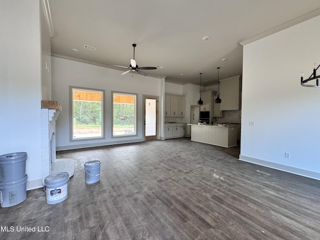 unfurnished living room with sink, ceiling fan, dark hardwood / wood-style floors, ornamental molding, and a brick fireplace