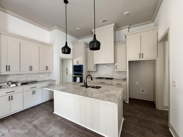 kitchen featuring sink, light stone counters, decorative light fixtures, black oven, and a kitchen island with sink