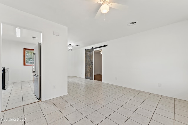 tiled spare room featuring ceiling fan and a barn door