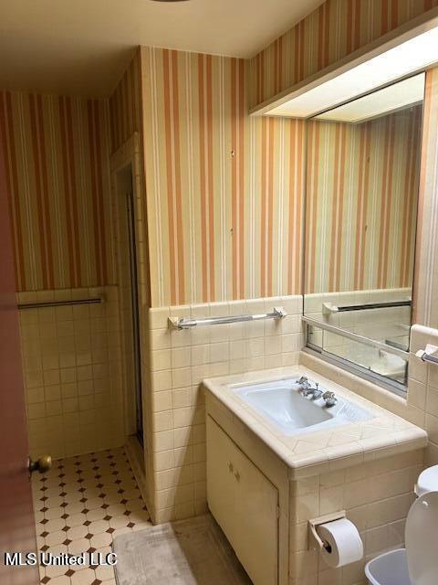 bathroom featuring wallpapered walls, tile patterned floors, a wainscoted wall, and tile walls