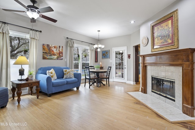 living area with light wood-style floors, a fireplace, baseboards, and ceiling fan with notable chandelier