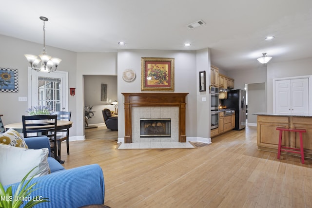 living room featuring a tile fireplace, baseboards, visible vents, and light wood finished floors