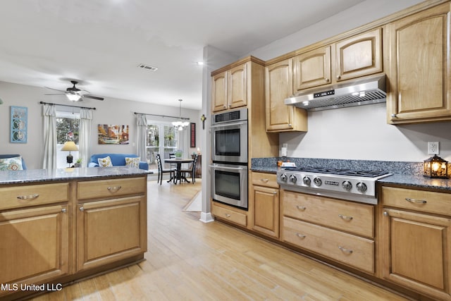 kitchen featuring visible vents, light wood-style flooring, dark stone countertops, stainless steel appliances, and under cabinet range hood