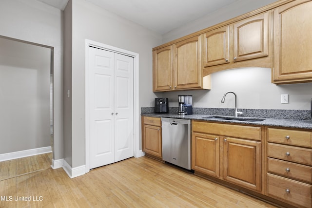 kitchen with stainless steel dishwasher, light wood-style floors, a sink, dark stone counters, and baseboards