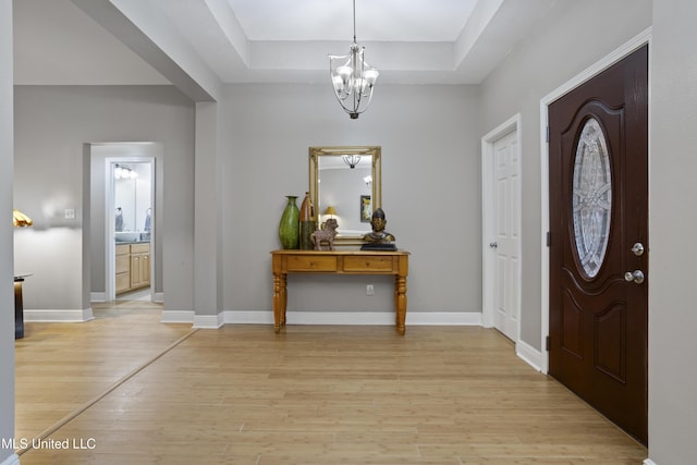 foyer featuring baseboards, a raised ceiling, light wood-style flooring, and an inviting chandelier