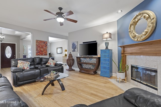 living room with ceiling fan with notable chandelier, a tile fireplace, wood finished floors, and baseboards