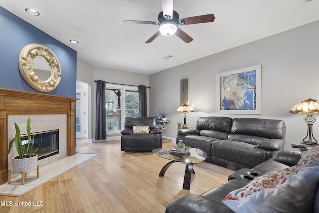 living area with visible vents, a tiled fireplace, a ceiling fan, wood finished floors, and baseboards