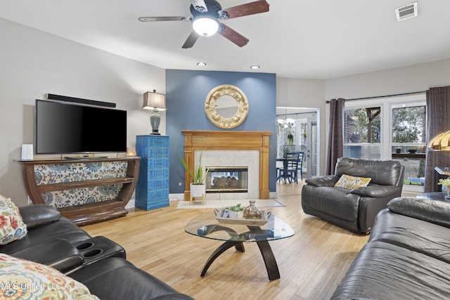 living area featuring baseboards, visible vents, a tile fireplace, wood finished floors, and ceiling fan with notable chandelier