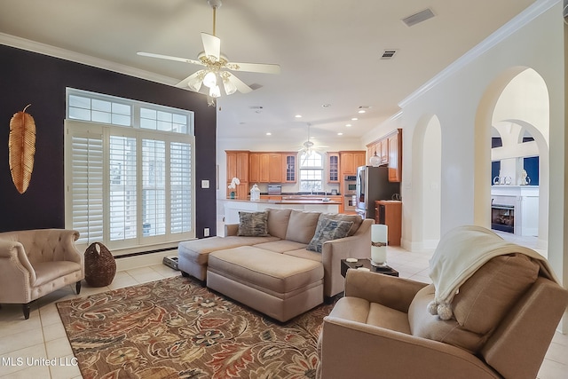 living area featuring light tile patterned floors, ceiling fan, arched walkways, ornamental molding, and a glass covered fireplace