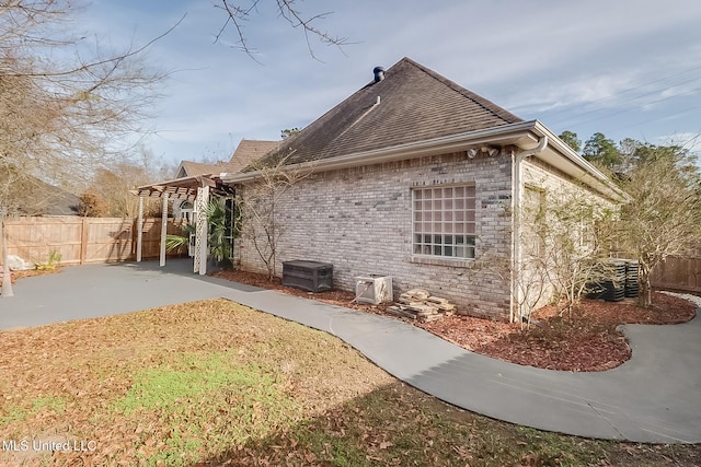 view of side of home featuring roof with shingles, brick siding, a patio, and fence