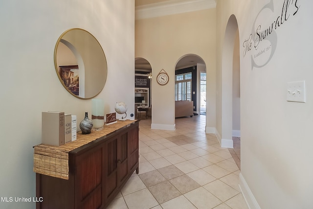 hallway featuring arched walkways, crown molding, light tile patterned floors, a high ceiling, and baseboards