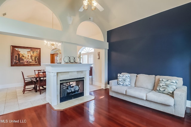 living area featuring baseboards, a ceiling fan, wood finished floors, a high ceiling, and a fireplace