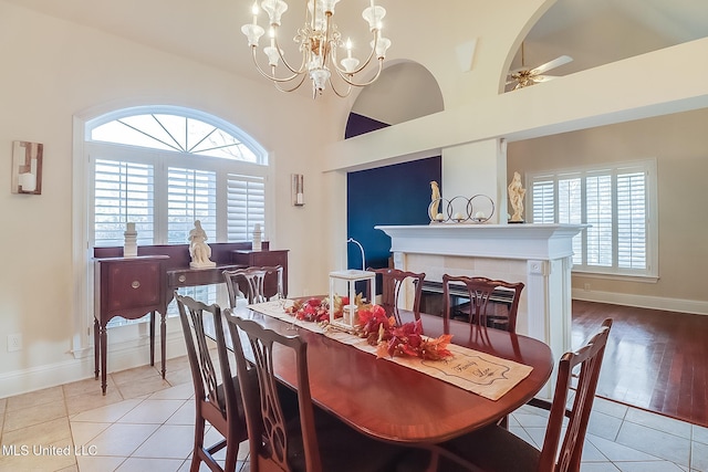 dining space with ceiling fan with notable chandelier, a high ceiling, baseboards, and light tile patterned floors