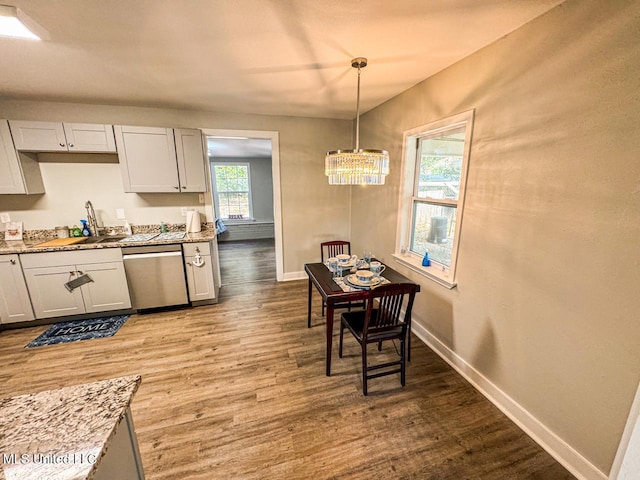 kitchen featuring sink, dishwasher, hanging light fixtures, hardwood / wood-style floors, and light stone counters