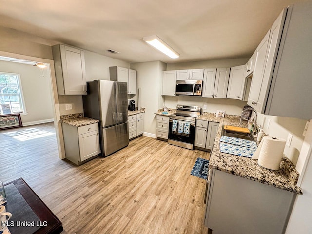 kitchen featuring gray cabinets, sink, light hardwood / wood-style floors, stainless steel appliances, and light stone countertops