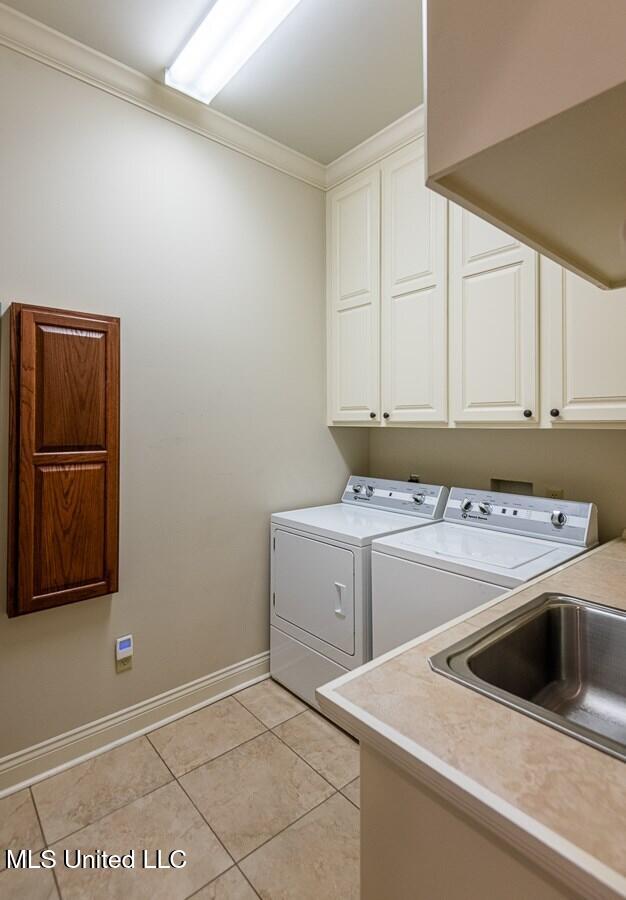 laundry area with cabinets, crown molding, sink, washer and dryer, and light tile patterned floors