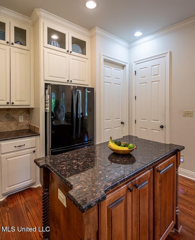 kitchen with black fridge, dark hardwood / wood-style flooring, backsplash, dark stone countertops, and white cabinets