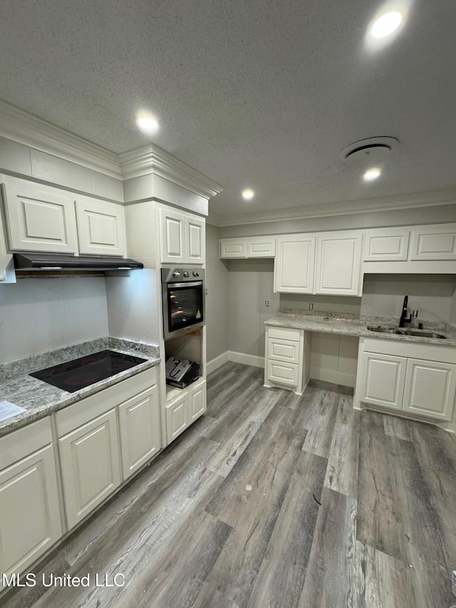 kitchen with light stone countertops, ornamental molding, light hardwood / wood-style floors, black electric cooktop, and stainless steel oven