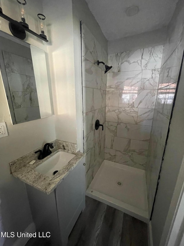 bathroom with wood-type flooring, tiled shower, and vanity