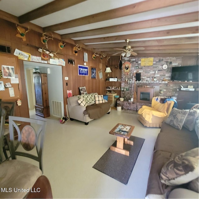 living area with wood walls, a ceiling fan, beamed ceiling, and visible vents