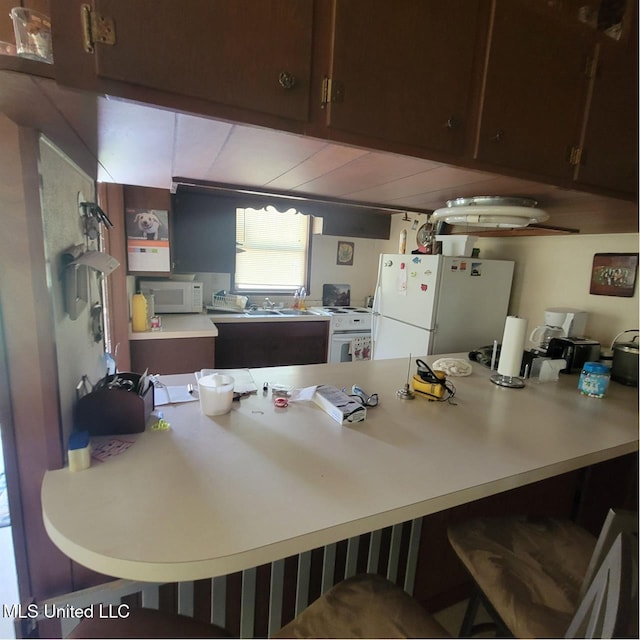 kitchen featuring light countertops, a peninsula, a kitchen breakfast bar, and white appliances