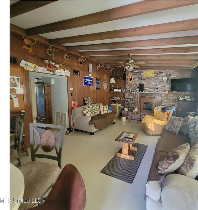 living area with beam ceiling, visible vents, ceiling fan, wooden walls, and a fireplace