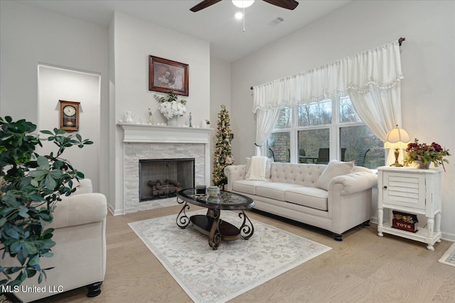 living room with ceiling fan, a stone fireplace, and light hardwood / wood-style flooring