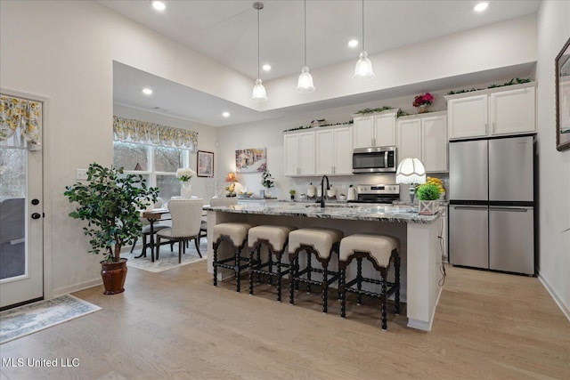 kitchen with a center island with sink, stone countertops, white cabinetry, and stainless steel appliances