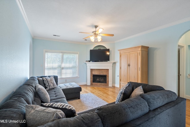 12857 Arbor Dr, Olive Branch, MS 38654 - living room featuring arched walkways, a ceiling fan, light wood finished floors, crown molding, and a tiled fireplace