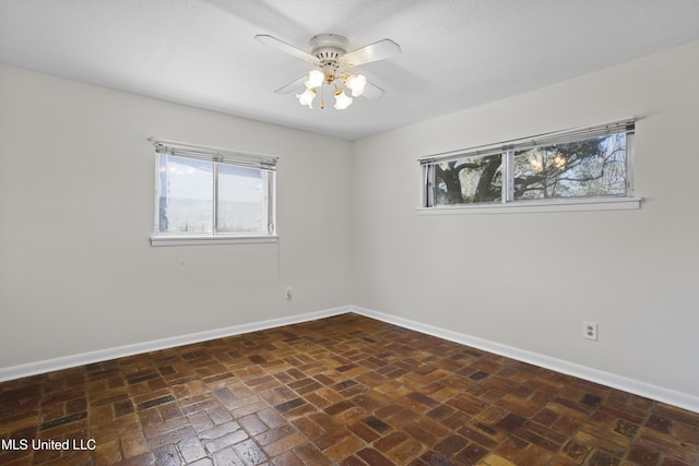 empty room featuring brick floor, baseboards, and a ceiling fan