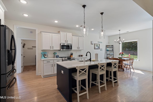 kitchen featuring appliances with stainless steel finishes, sink, an island with sink, hanging light fixtures, and white cabinets