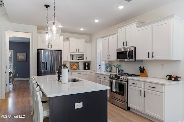 kitchen with appliances with stainless steel finishes, an island with sink, white cabinets, and pendant lighting