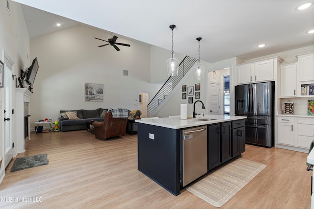 kitchen featuring white cabinetry, stainless steel appliances, high vaulted ceiling, light hardwood / wood-style flooring, and a center island with sink