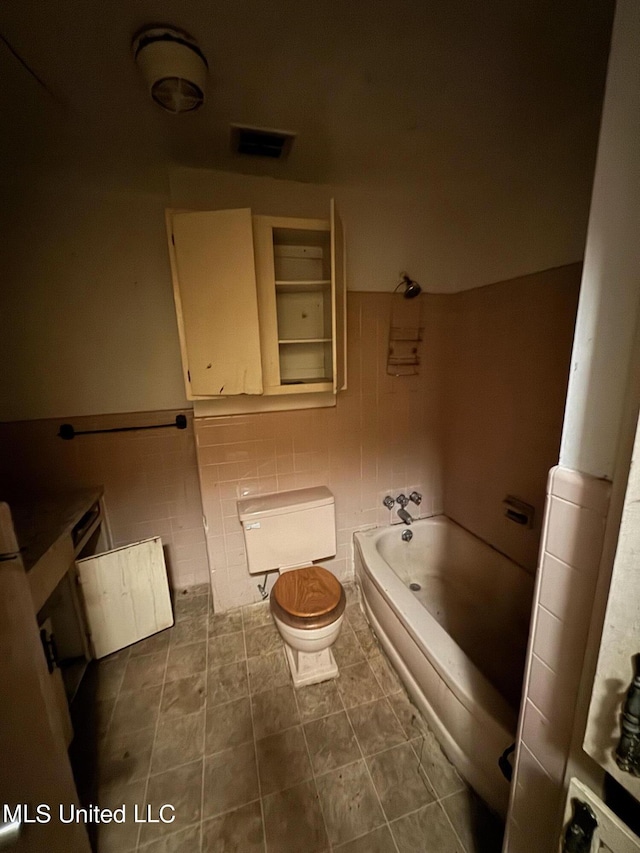 bathroom featuring tile patterned floors, a tub, tile walls, and toilet