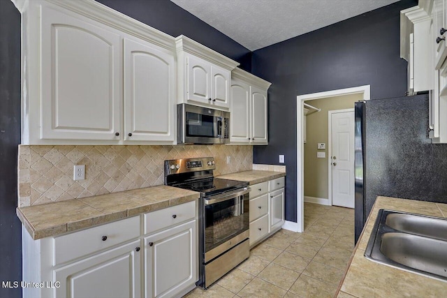 kitchen featuring a sink, appliances with stainless steel finishes, light tile patterned floors, and backsplash